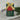 A Christmas-themed scented soap bar wrapped in dark green paper with gold foil lettering reading 'JOYFUL' and a red label that says 'CHRISTMAS FOLIAGE,' tied with a gold ribbon, set on a textured cream fabric with evergreen branches in the background.