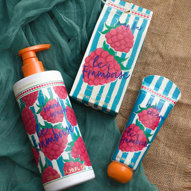 Hand wash, cream, and packaging with raspberry design on a textured fabric background