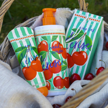 Cherry-themed hand wash and soap bars in a basket with greenery in the background