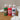 Three Sing-Along Hand Sanitizer bottles with pump dispensers are lined up on a wooden bathroom counter next to a white sink and towels. The bottles are decorated with festive Christmas illustrations: a green elf bottle labeled 'Candy Apple', a red Santa bottle labeled 'Candy Cane', and a white snowman bottle labeled 'Spiced Tea'.