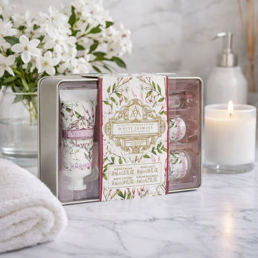 Set of White Jasmine hand cream and body lotion in a decorative tin with flowers and candles in the background.