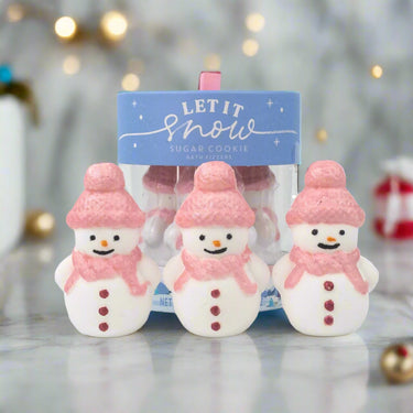 Three snowman-shaped cookies with pink hats and scarves in front of a 'Let It Snow' package.