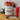 Naturally European Spiced Pomegranate Scented Pampering Collection gift set on a wooden table, featuring a red and gold patterned body mist tin, a clear body wash bottle, a red hand cream tube, and a small spray bottle.